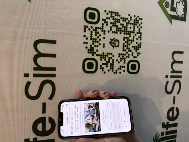Hand holding a phone in front of a Dreamlife-Sim™ banner with QR code